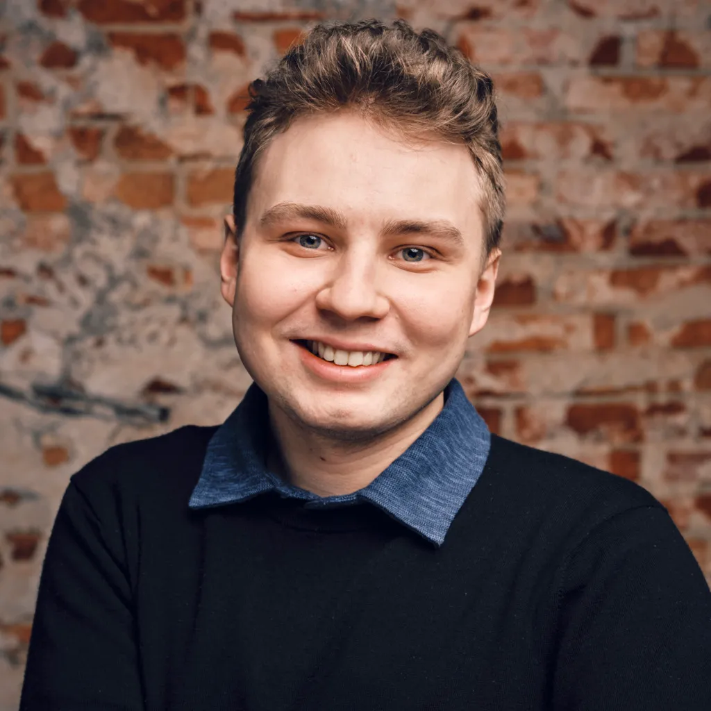 Mikael Siidorow smiling in front of a brick wall